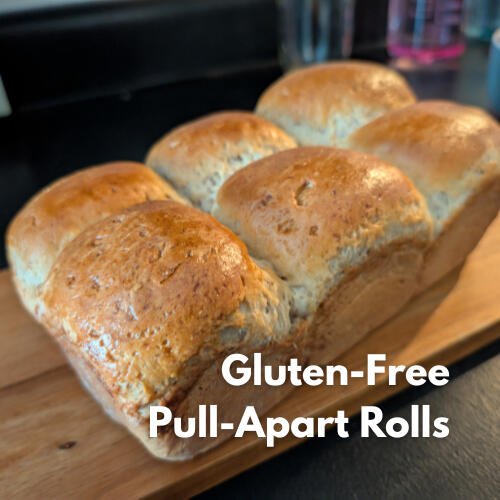 Gluten-free pull-apart dinner rolls resting on a cutting board, brushed with melted butter.
